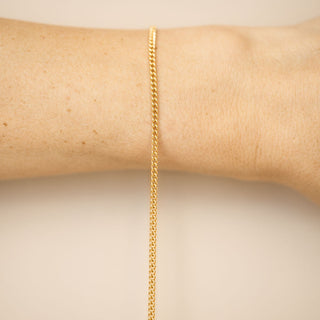 Gold chain bracelet on a wrist against a beige background