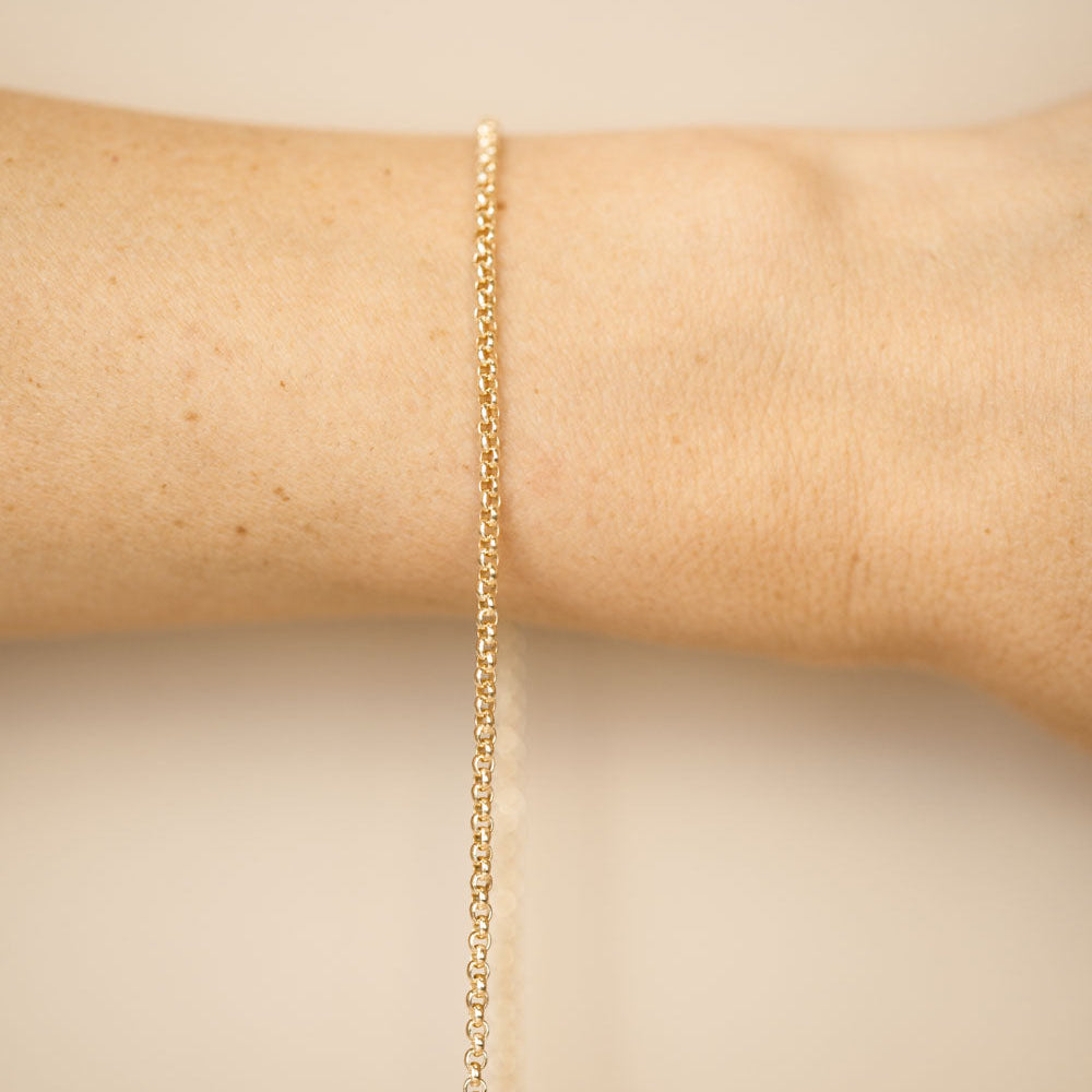 Gold bracelet on a wrist against a beige background