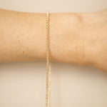 Gold bracelet on a wrist against a beige background