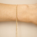 Gold bracelet on a wrist against a beige background