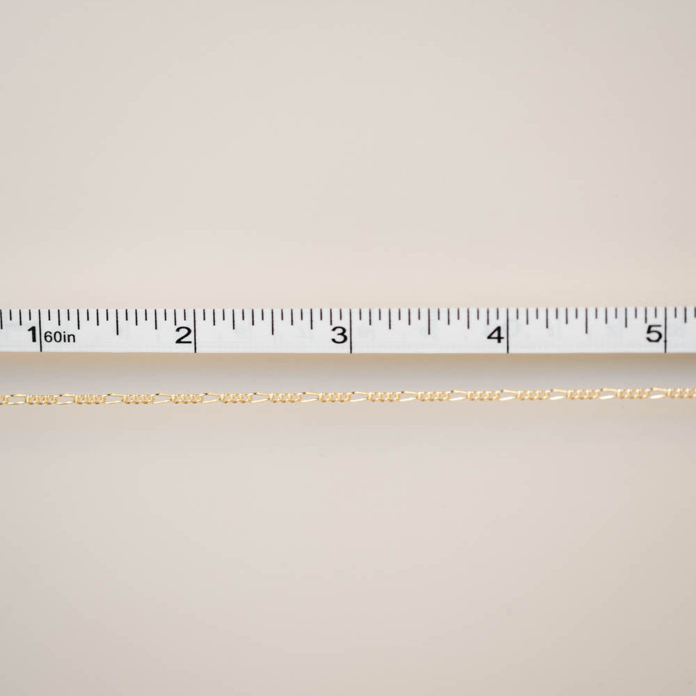 Gold chain with a ruler for scale on a beige background