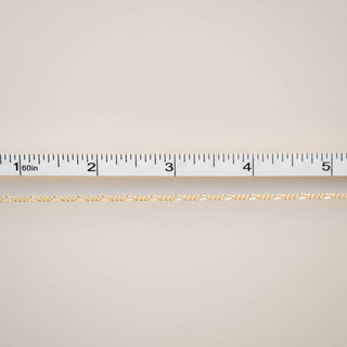 Gold chain with a ruler for scale on a beige background