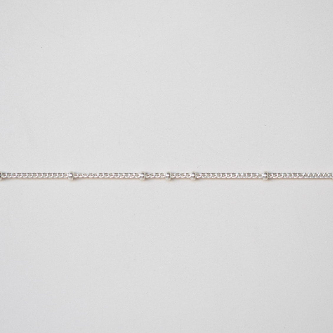 Thin silver chain on a light gray background