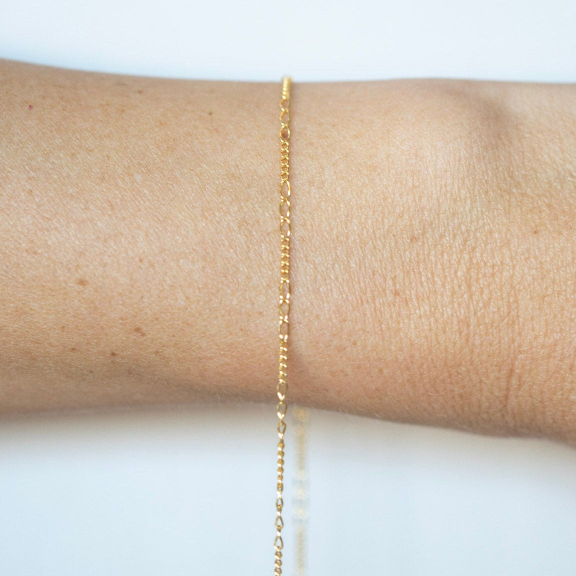 Gold bracelet on a person's wrist against a white background