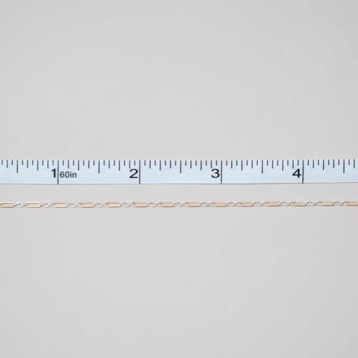 Thin beige thread on a white background with a ruler for scale.