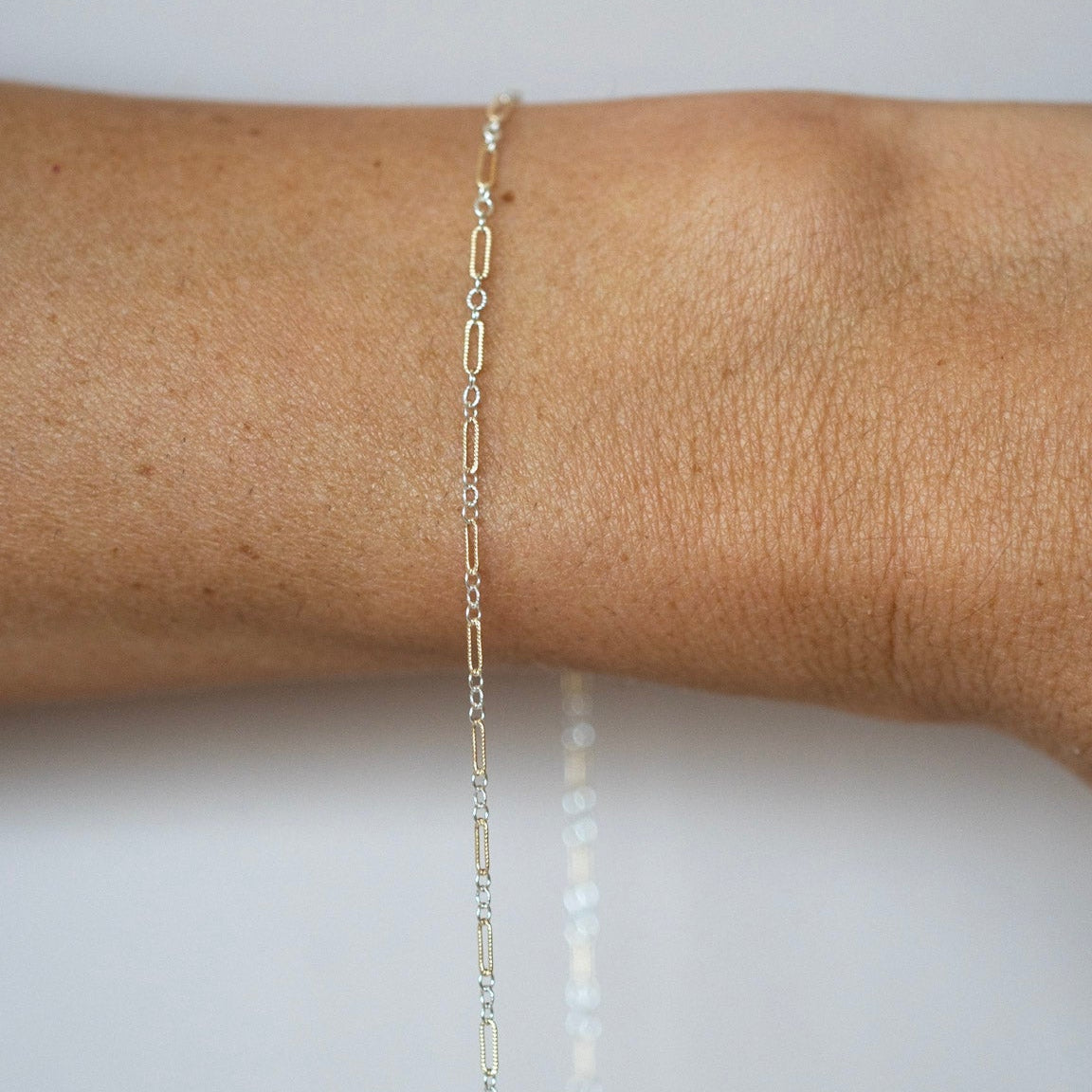 Gold chain bracelet on a wrist against a white background