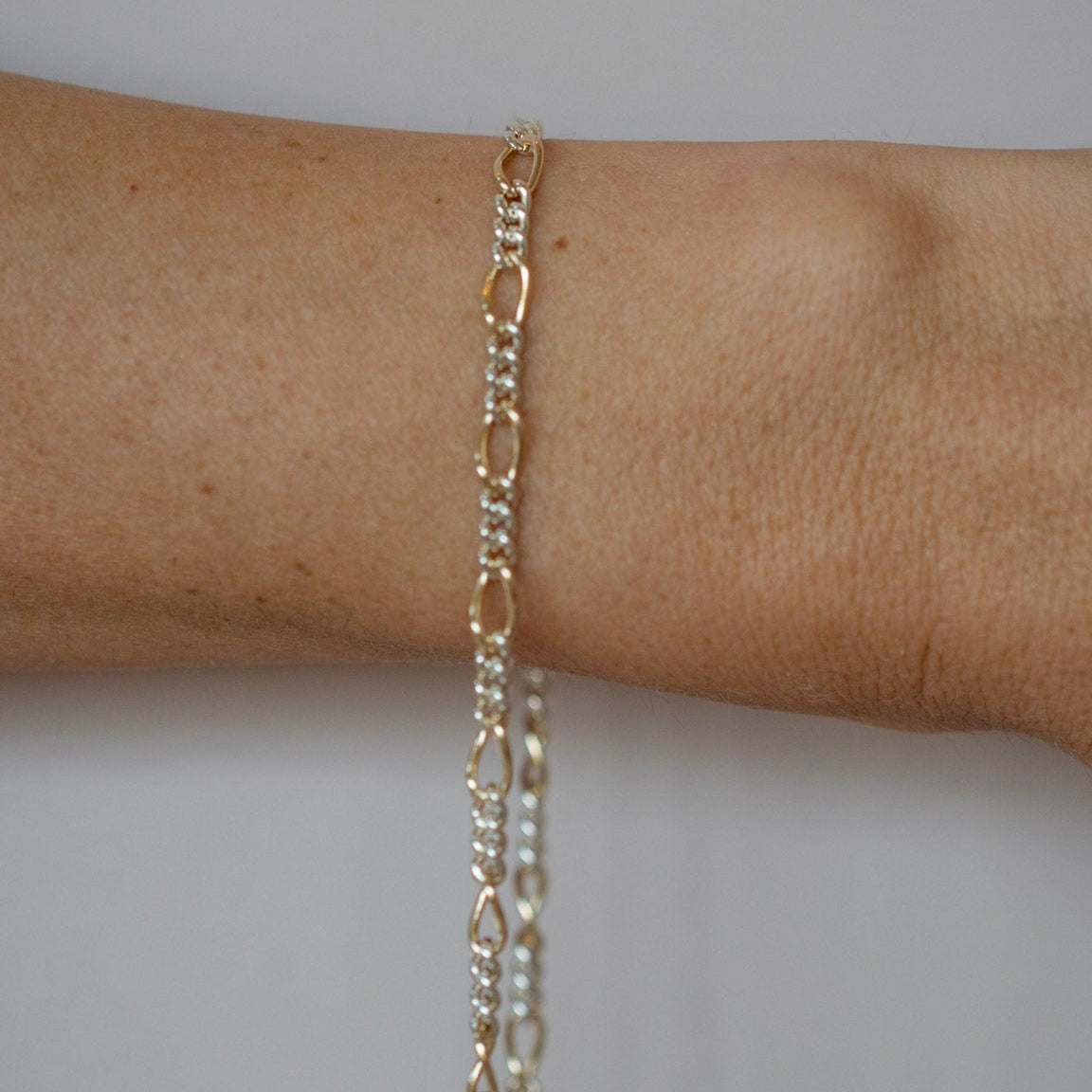 Gold chain bracelet on a person's wrist against a neutral background