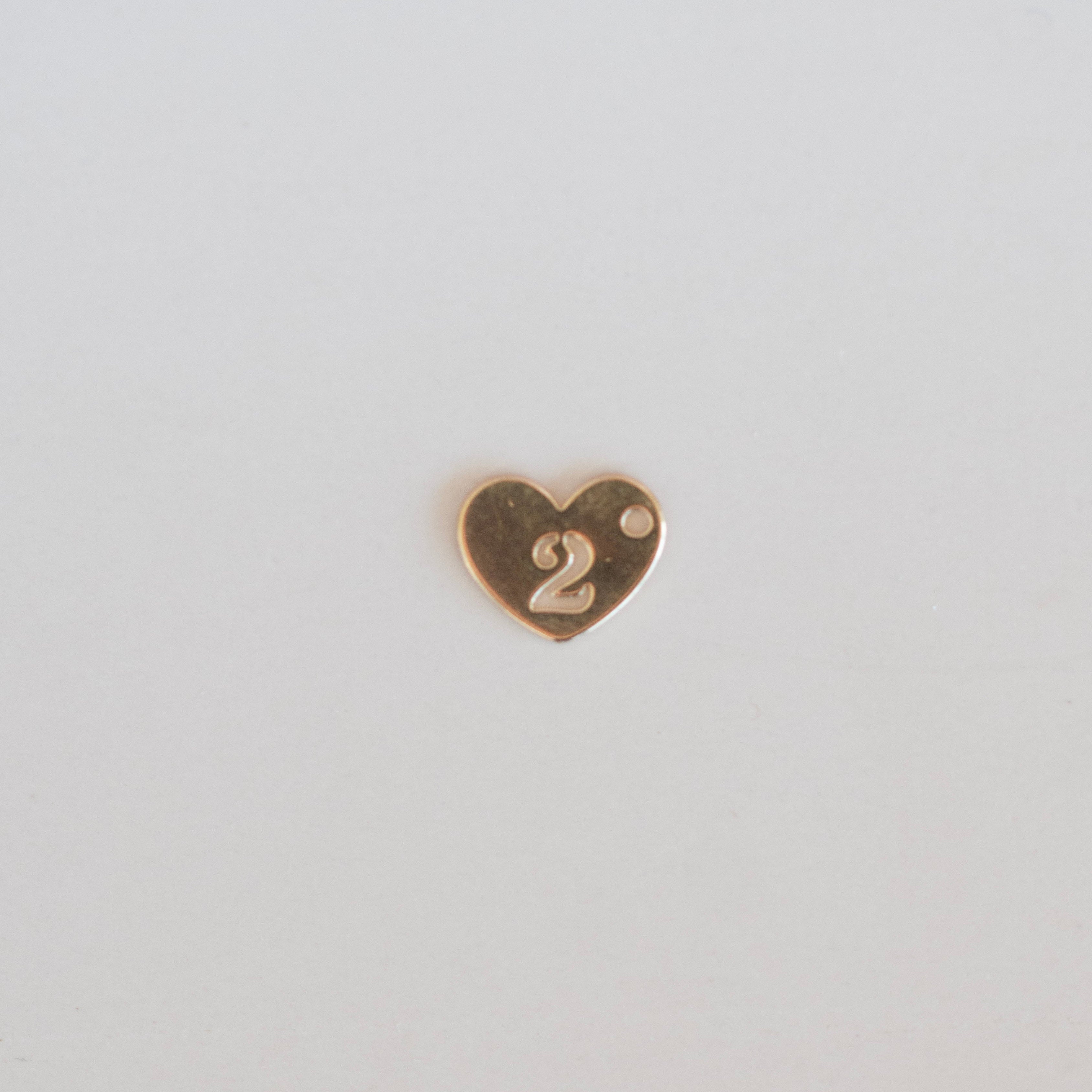 Gold heart-shaped number '2' charm on a light gray background