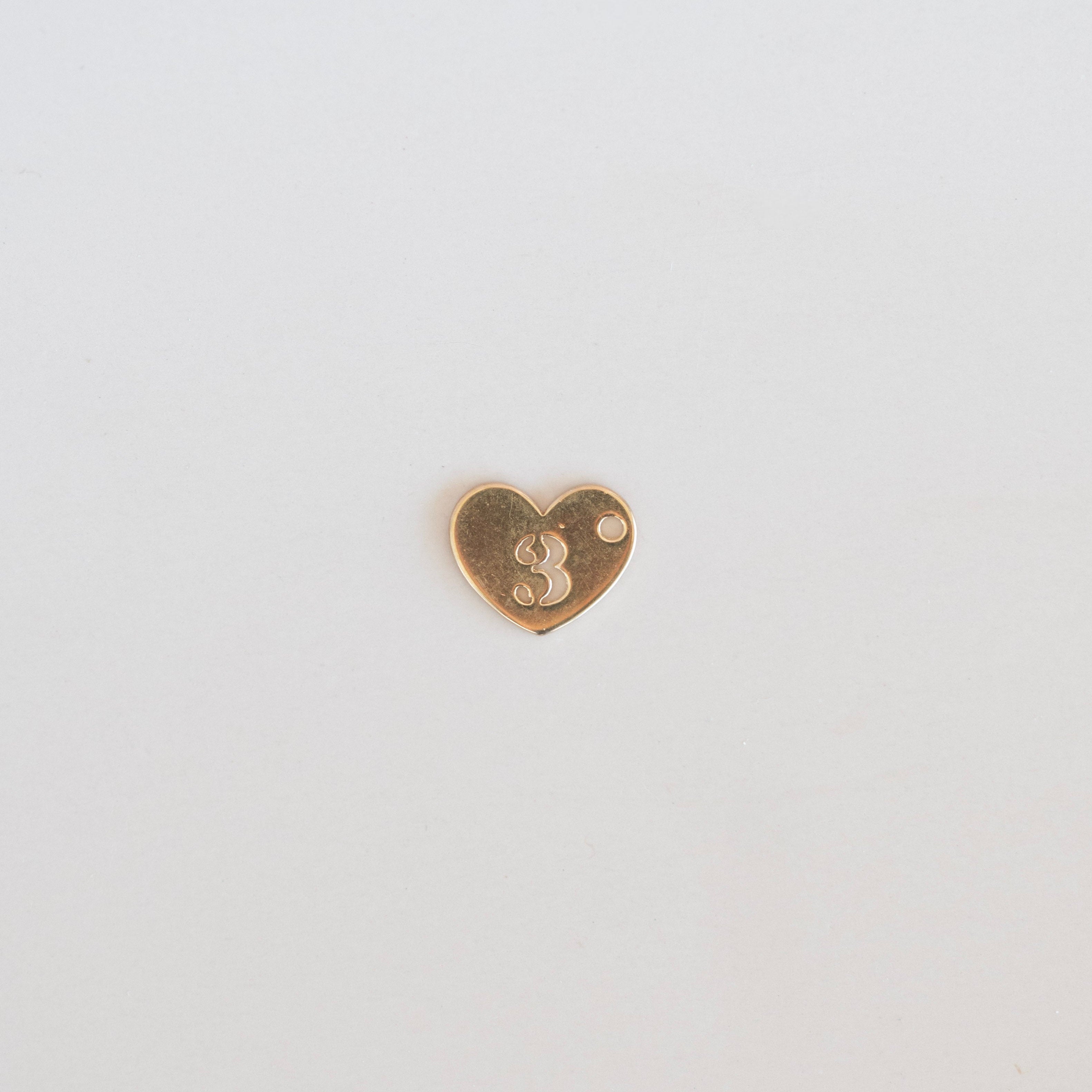Heart-shaped gold charm with the number 3 on a light gray background