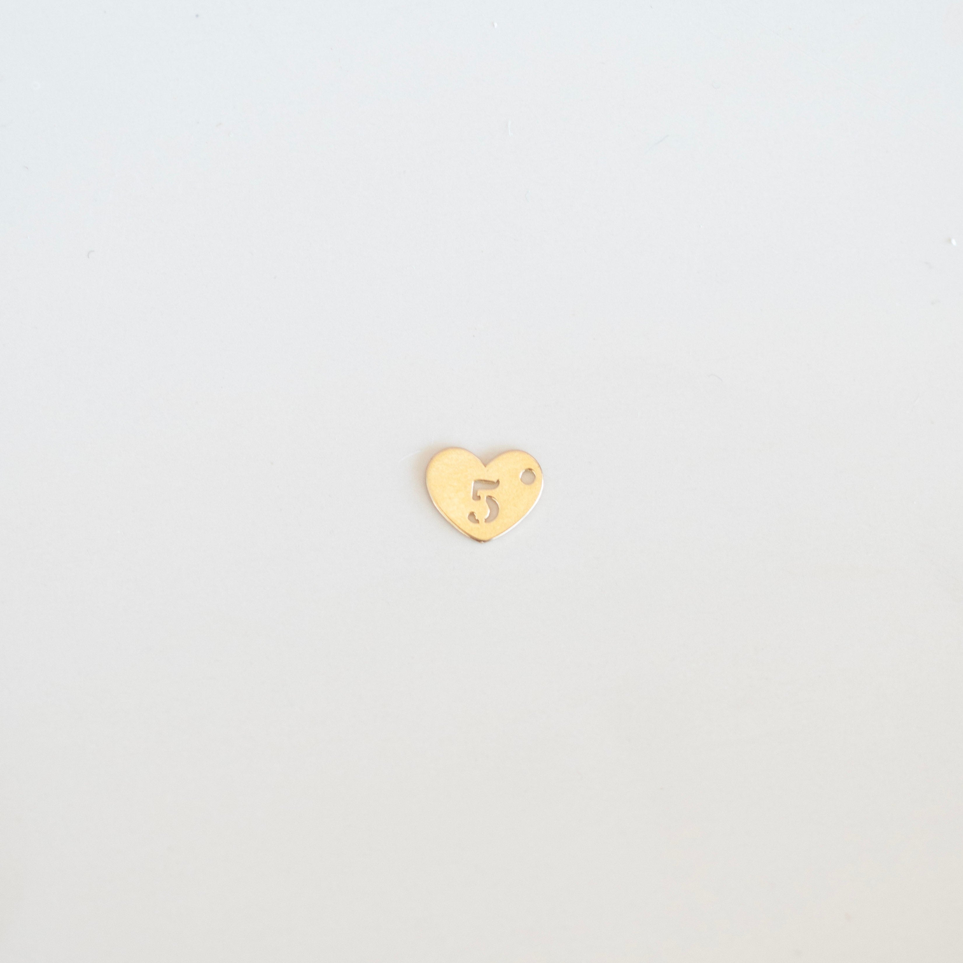 Gold heart-shaped charm with a number '5' on a light gray background