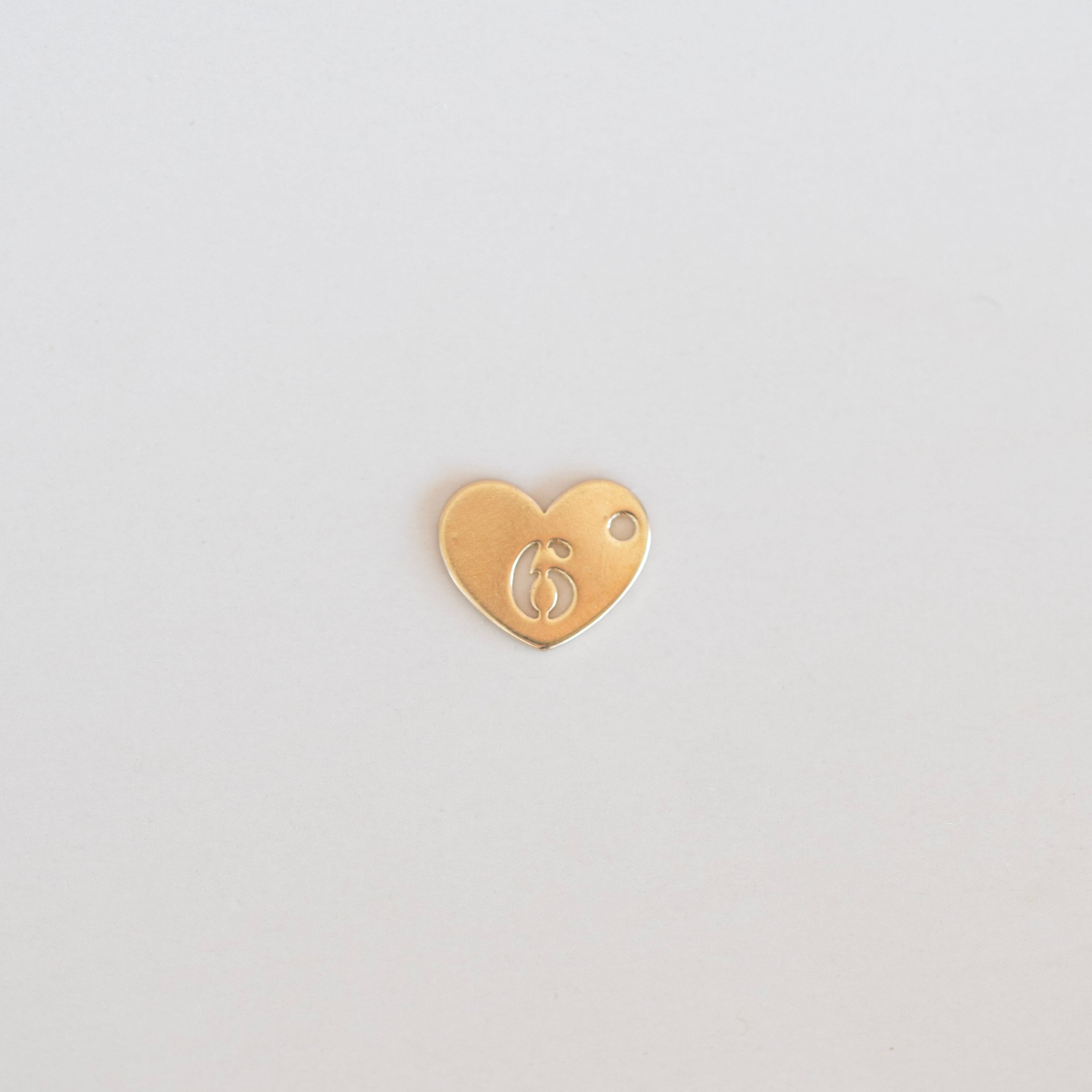 Gold heart-shaped charm with number 6 on a light gray background