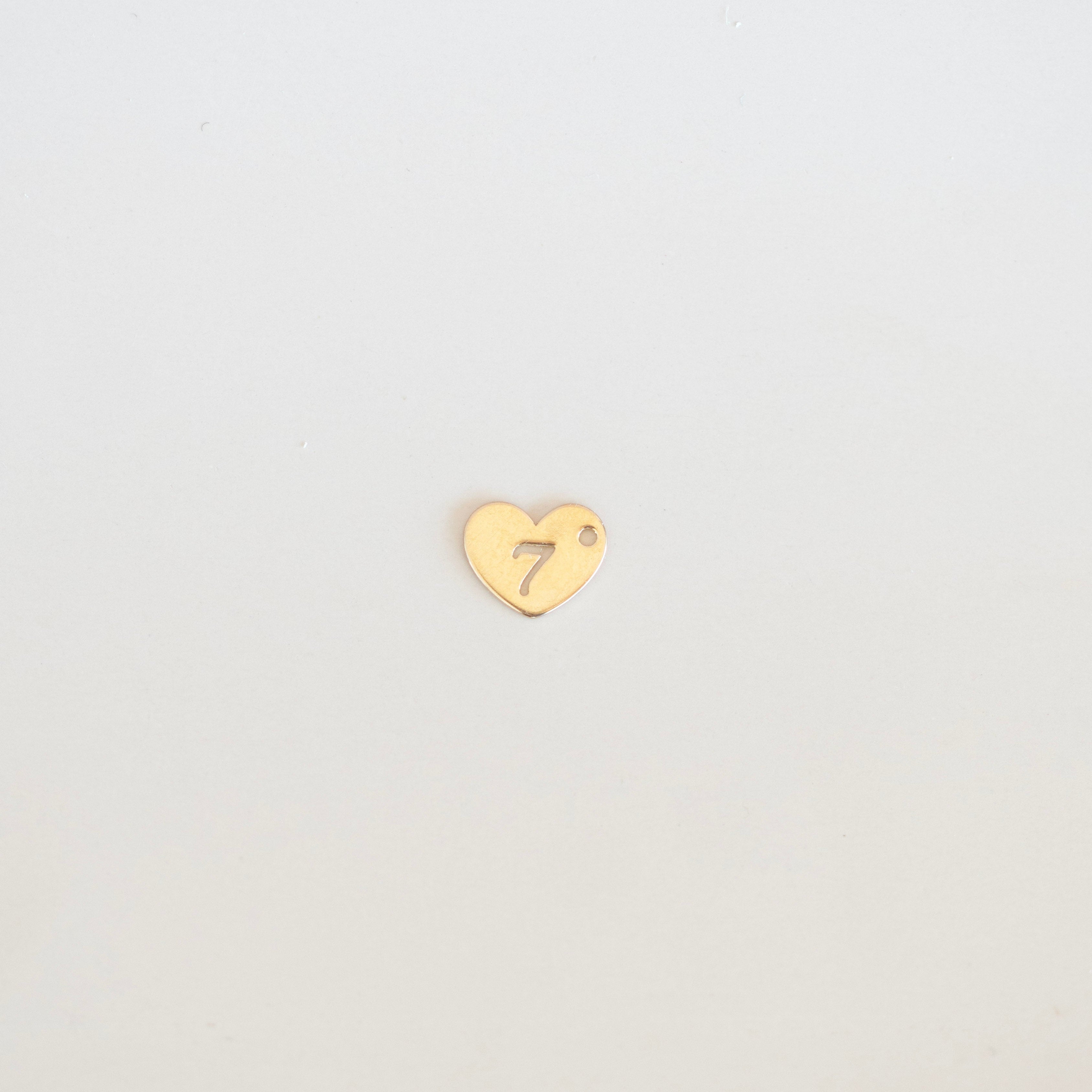 Gold heart-shaped charm with a number '7' on a light gray background