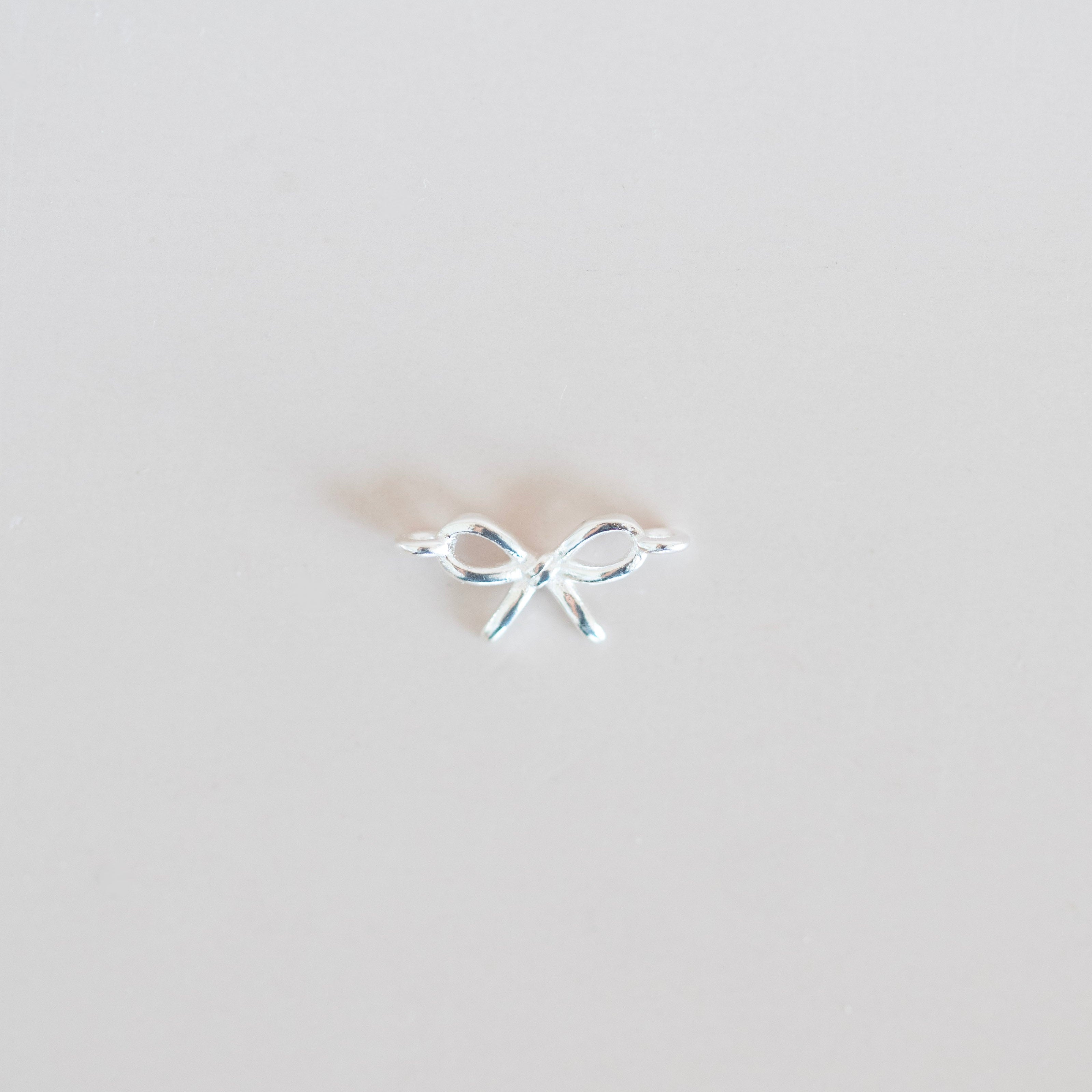 Small silver bow-shaped earring on a light gray background