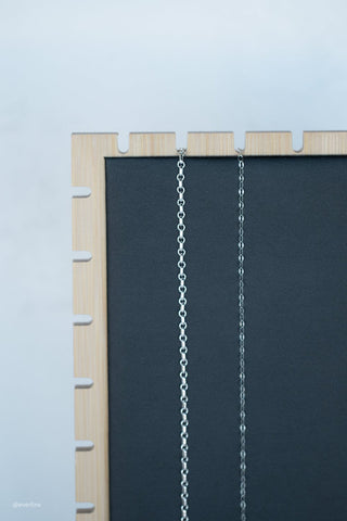 Two silver chains hanging in front of a dark background.