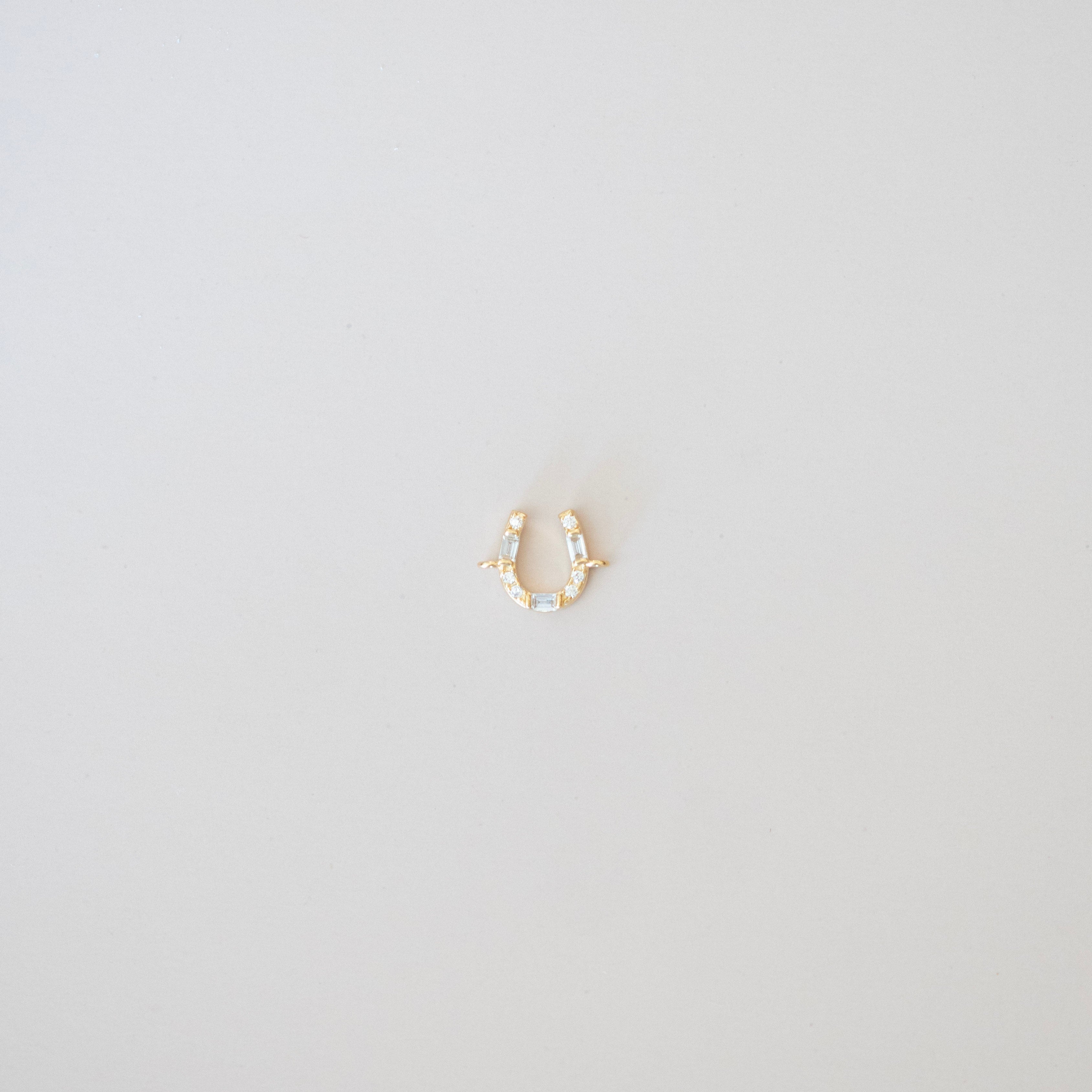Gold horseshoe-shaped earring on a light gray background