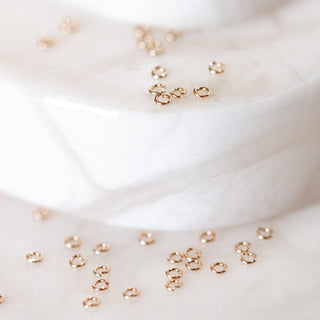 Gold jump rings scattered on white surfaces.