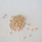 Small gold beads scattered on a light gray background