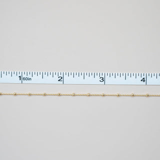 Gold chain next to a ruler on a light gray background