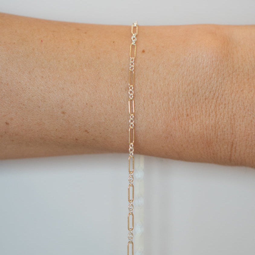 Gold chain bracelet on a person's wrist against a light gray background