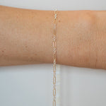 Gold chain bracelet on a person's wrist against a light gray background