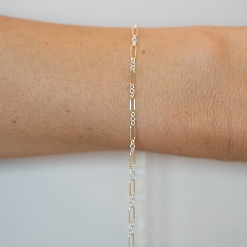 Gold bracelet on a person's wrist against a light gray background