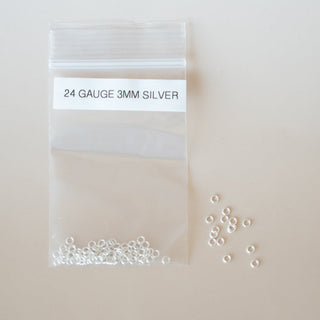 Small clear plastic bag with silver beads labeled '24 Gauge 3MM Silver' on a light beige background.