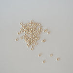 Small gold jump rings scattered on a light gray background