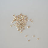 Small gold jump rings scattered on a light gray background