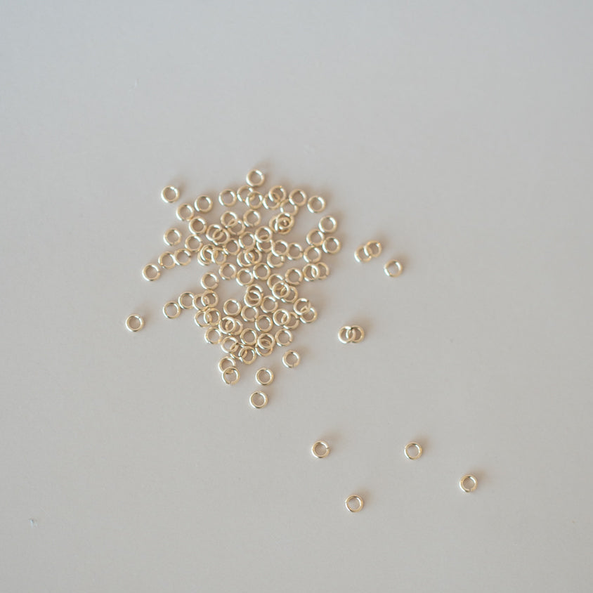 Small gold jump rings scattered on a light gray background