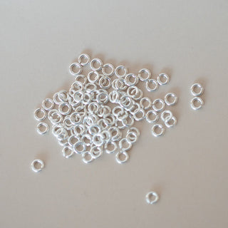 Small silver 22 gauge 3mm jump rings scattered on a light gray background
