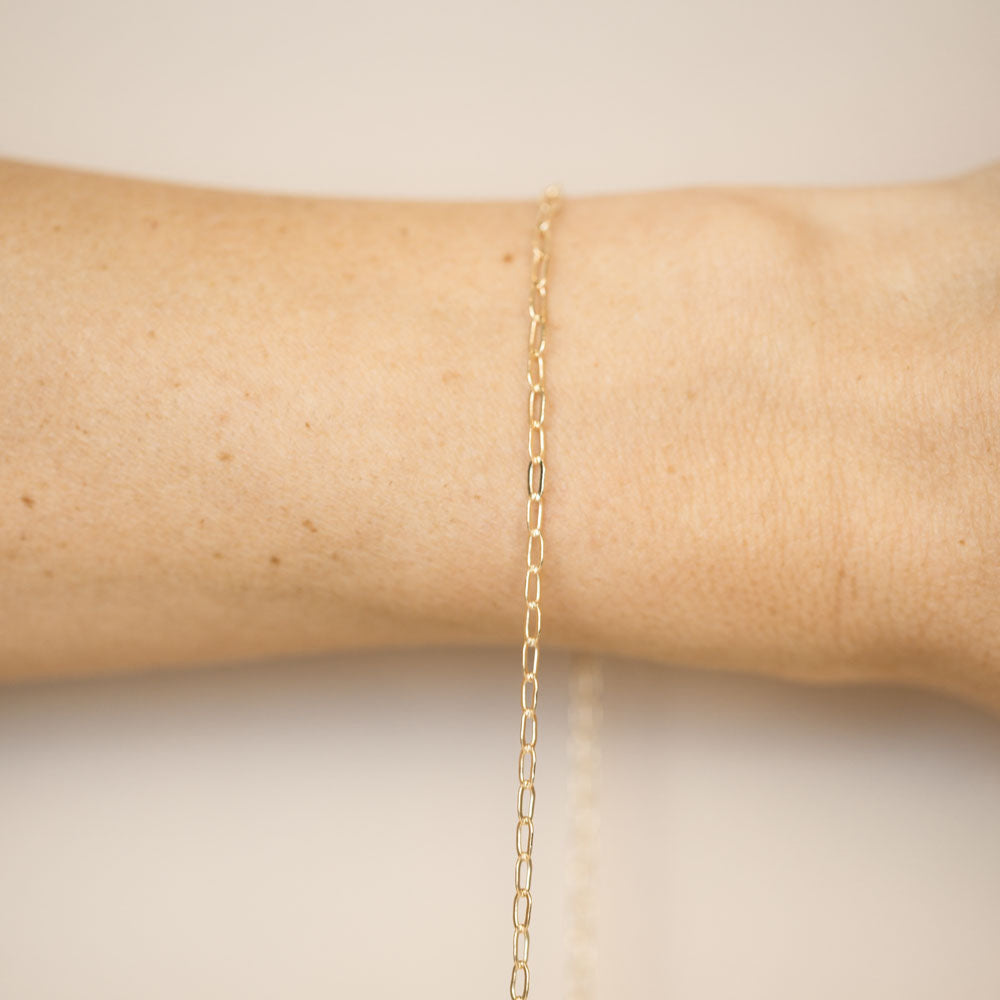 Gold chain bracelet on a wrist against a beige background