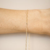 Gold chain bracelet on a wrist against a beige background
