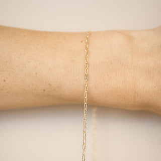 Gold chain bracelet on a wrist against a beige background