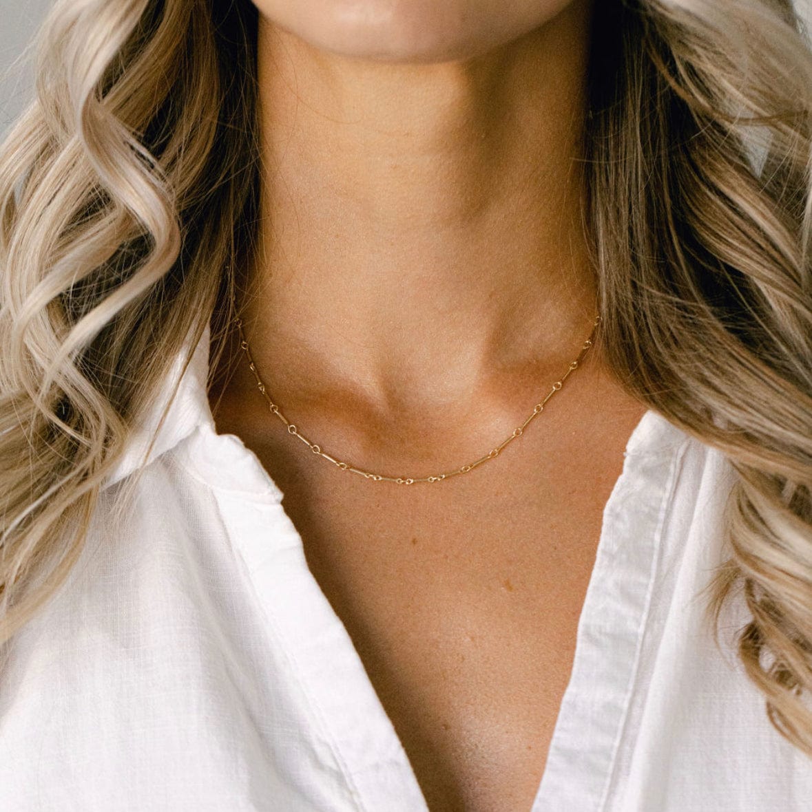 Woman wearing gold necklace and white shirt