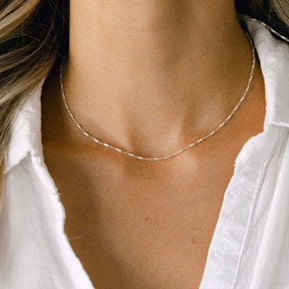 Delicate gold necklace on woman in white shirt.