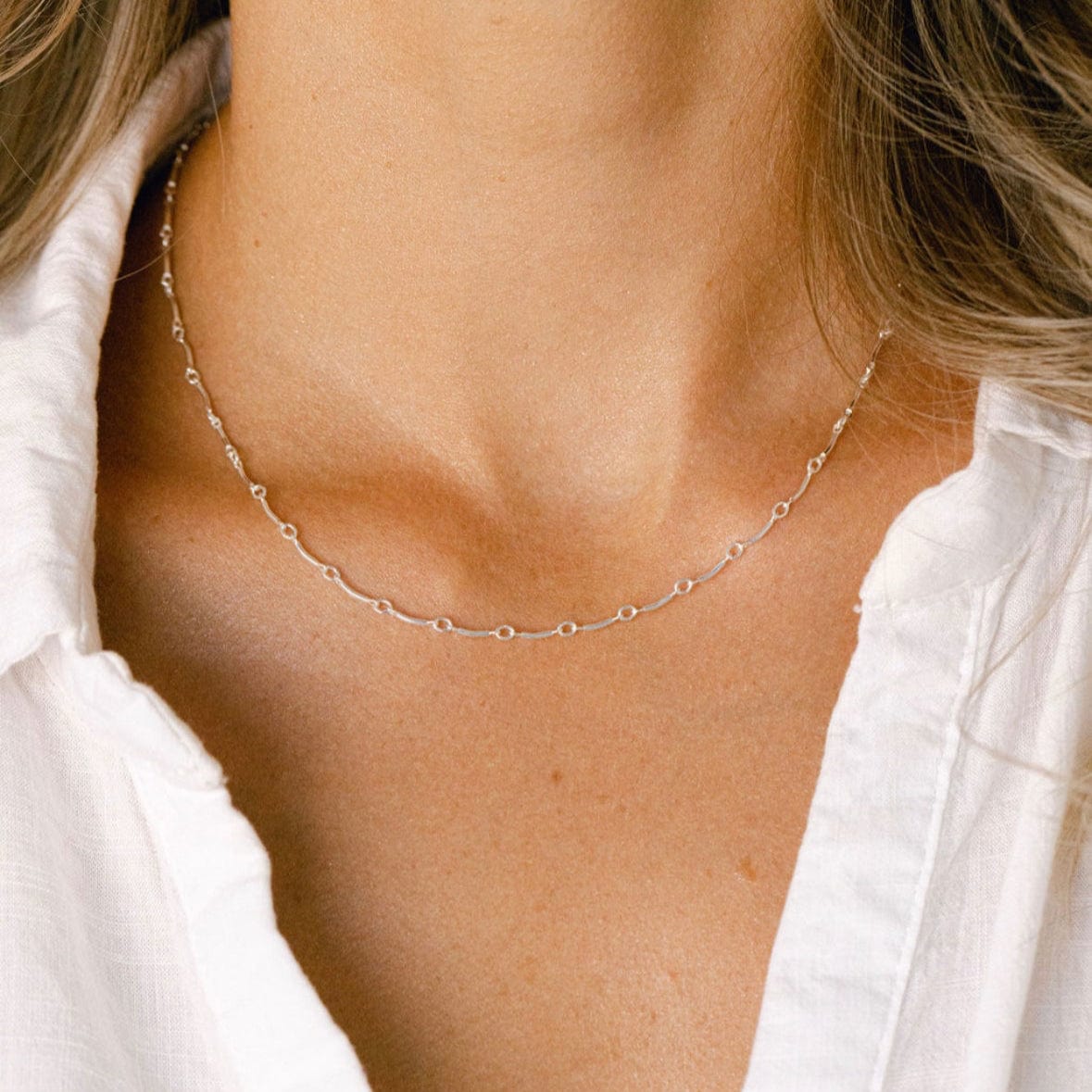 Gold beaded necklace on woman in white shirt