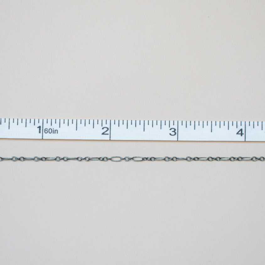 Silver chain next to a ruler on a light gray background