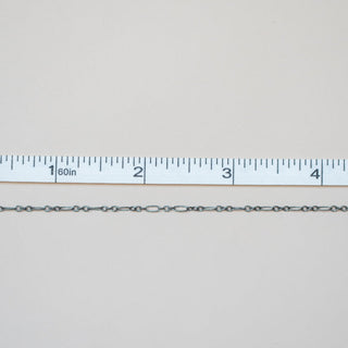 Silver chain next to a ruler on a light gray background