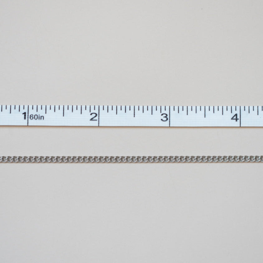 Metallic chain with a ruler for scale on a light gray background