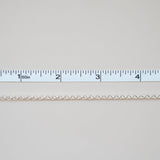Thin white chain on a light gray background with a ruler for scale.