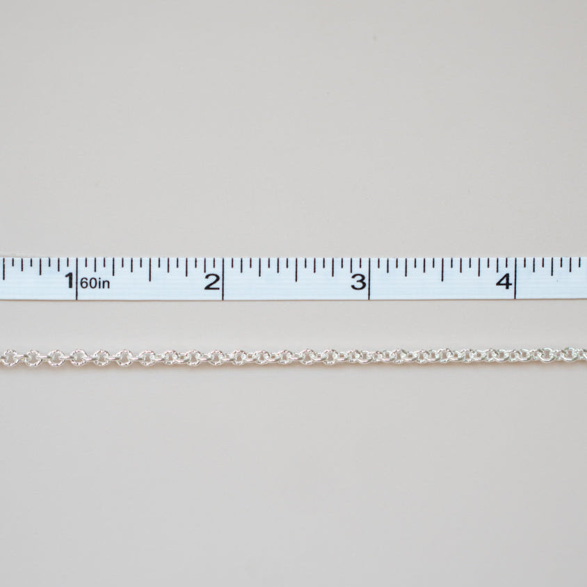 Thin white chain on a light gray background with a ruler for scale.