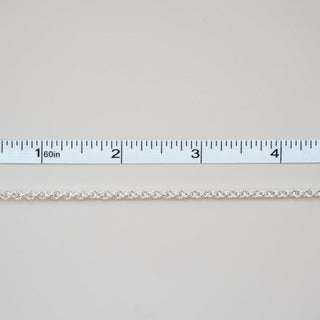 Thin white chain on a light gray background with a ruler for scale.
