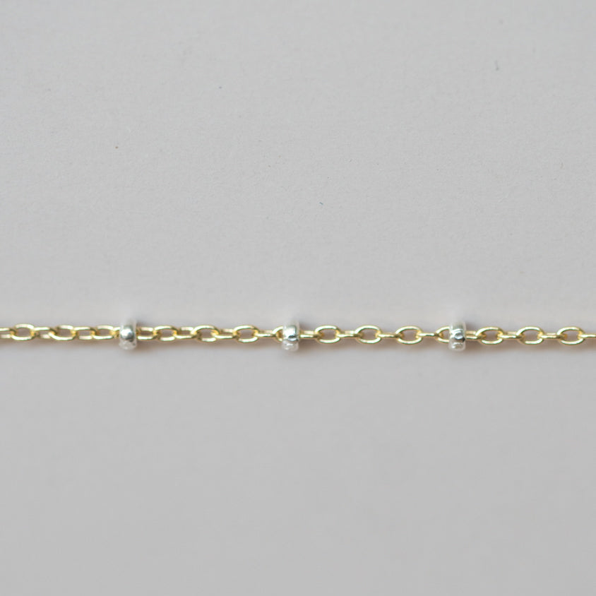 Gold bracelet with small beads on a light gray background