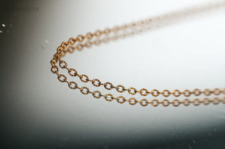 Gold chain necklace reflecting on a surface.
