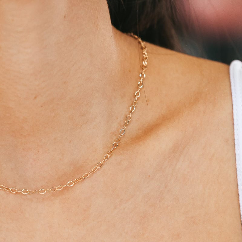 Woman's neck and shoulder with a gold chain necklace.